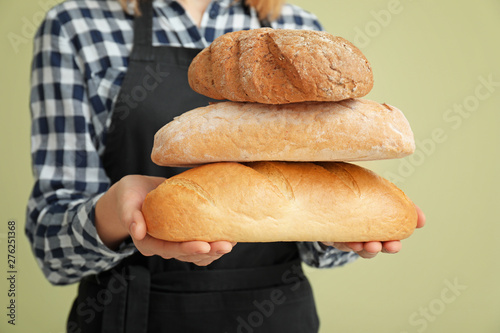 Female baker with bread on color background, closeup