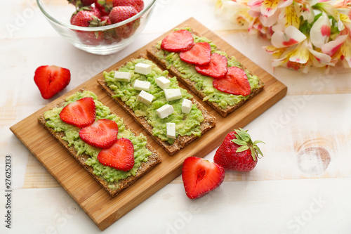 Wooden board with tasty avocado toasts on light table