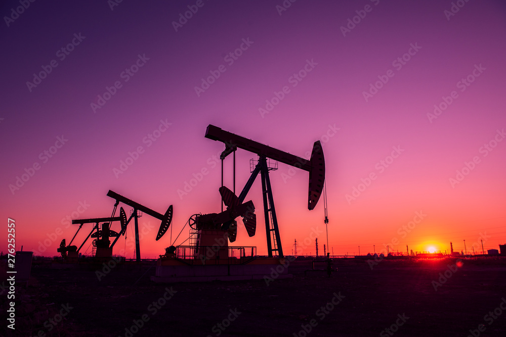 Oil pumps are running in the sunset at the oil field.