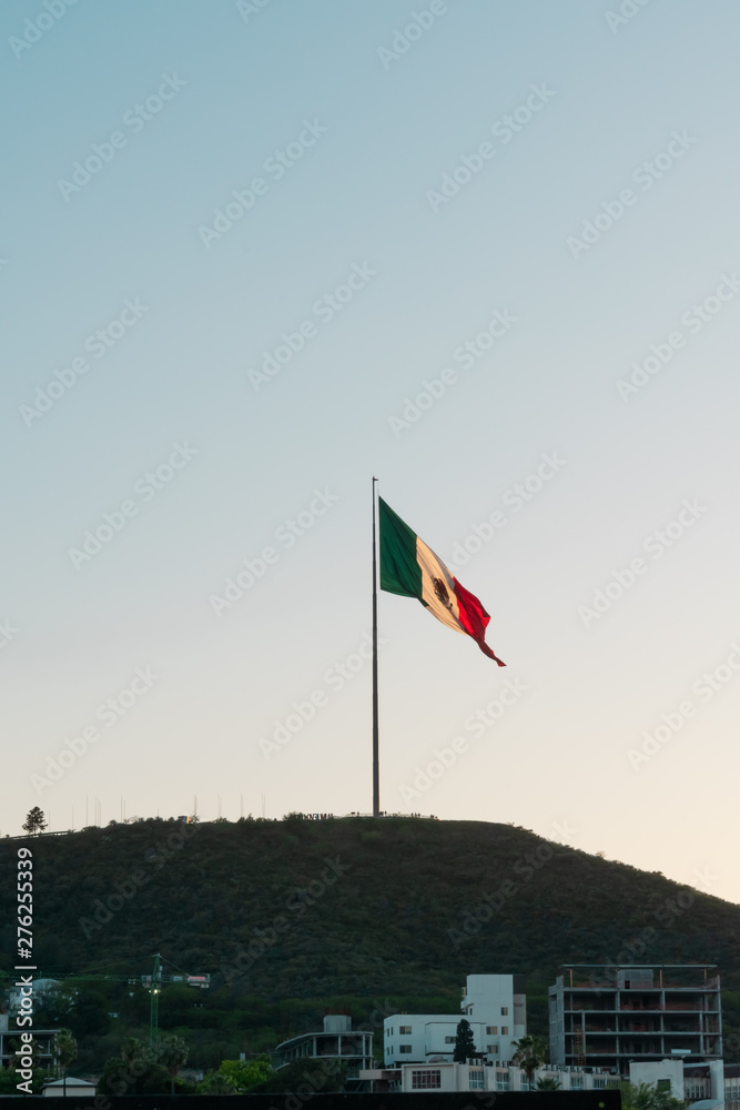 Mexican flag waving in the wind atop a hill during sunset on a clear day