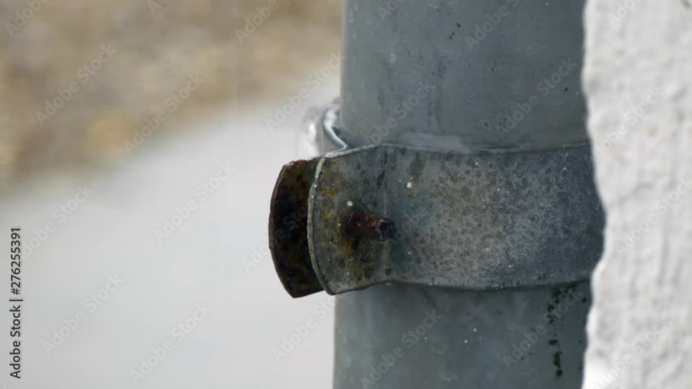 Zoom in on water running down a rusty screw on a grey zinc down spout on a rainy summer day