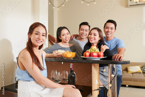 Group of happy young Asian men and women looking at their female friend who is hosting party at home