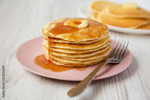 Stack of homemade pancakes with butter and maple syrup on a pink plate, side view. Closeup.