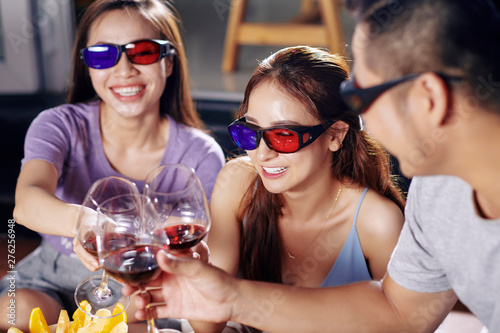 Happy young men and women in 3D glasses laughing and drinking wine when watching movie together © DragonImages