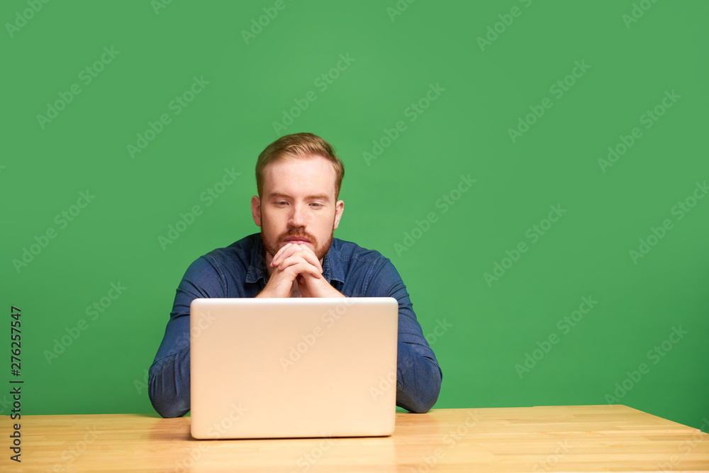 Pensive red-haired young Irish man looking at laptop screen and waiting when file is uploading Pensive red-haired young Irish man looking at laptop screen and waiting when file is uploading