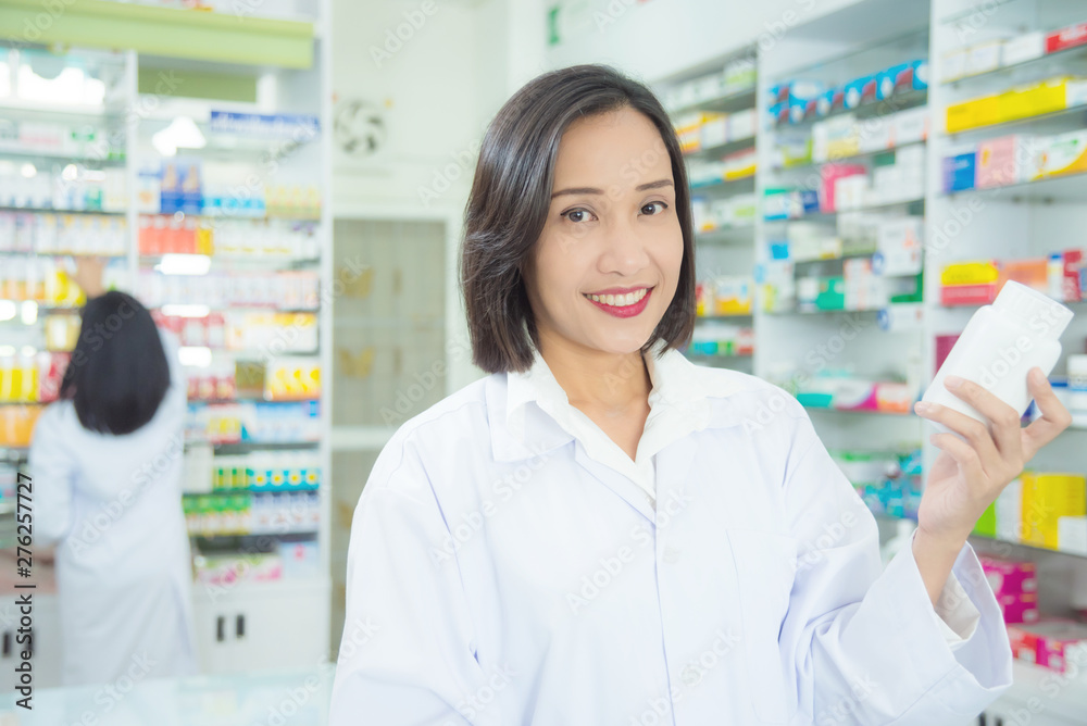 Smiling asian female pharmacist standing in pharmacy (chemist shop or drugstore)