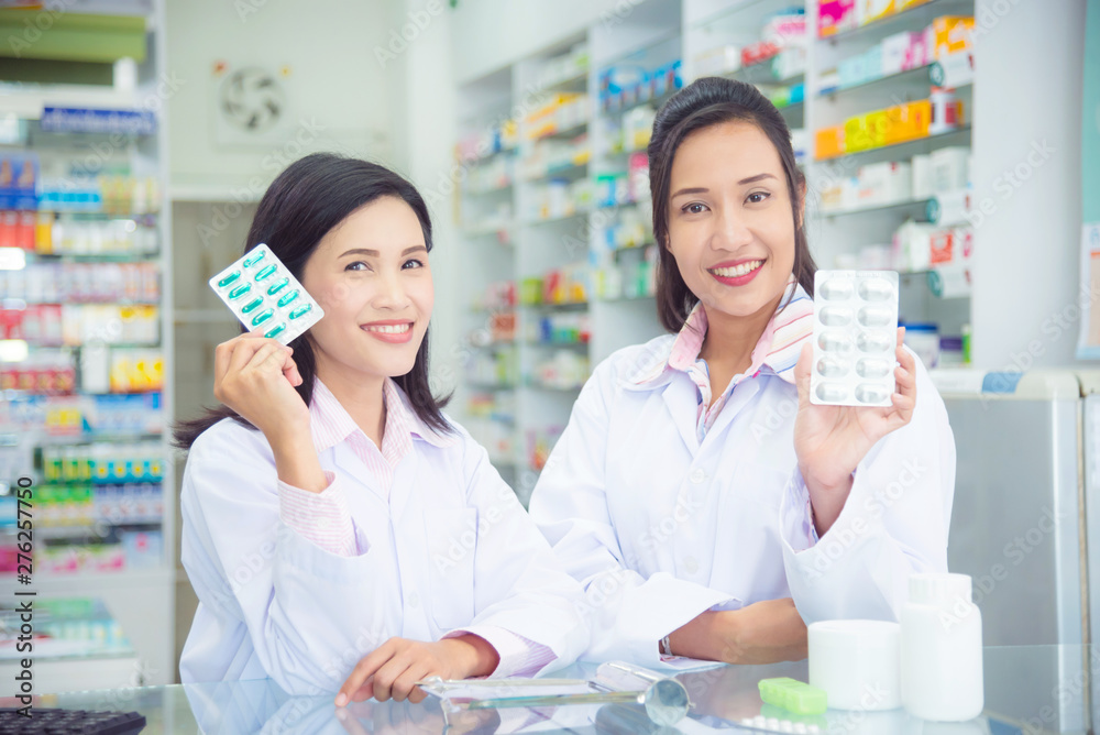 Two asian female pharmacist holding medicine and smile in pharmacy (chemist shop or drugstore)