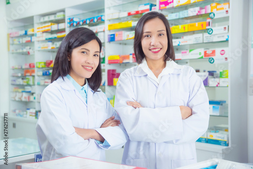 Two asian female pharmacist standing and smiling in pharmacy (chemist shop or drugstore)