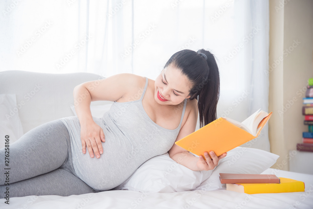 Beautiful asian pregnant woman lying on bed and reading book,touching her belly and smiling.Pregnant woman health concept. Beautiful asian pregnant woman lying on bed and reading book,touching her belly and smiling.Pregnant woman health concept.