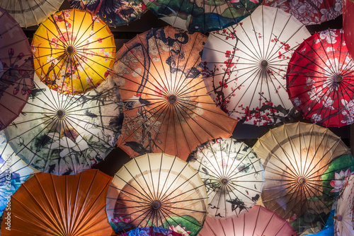 Multi colored chinese umbrellas hanging on a wall illuminated at night