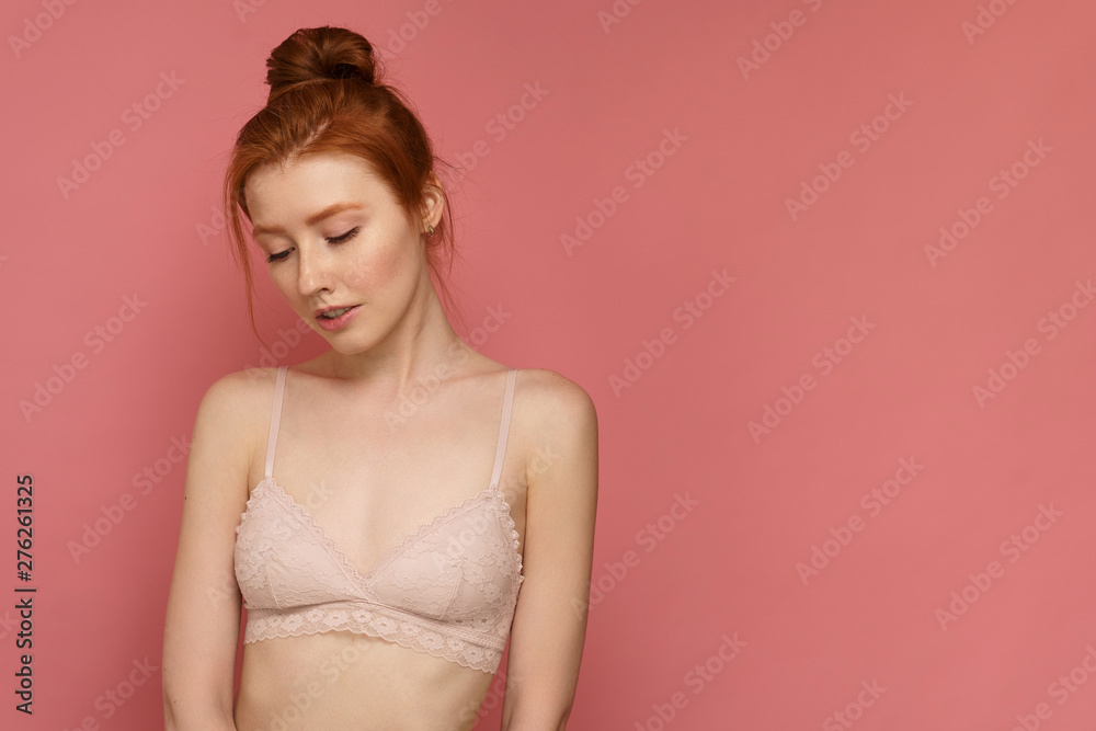 Young redhead woman wearing lace bra with a bun on her head looks down thinking about something Young redhead woman wearing lace bra with a bun on her head looks down thinking about something