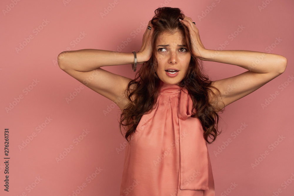 Young dark-haired woman clutches at her head looking up, pink background Young dark-haired woman clutches at her head looking up, pink background