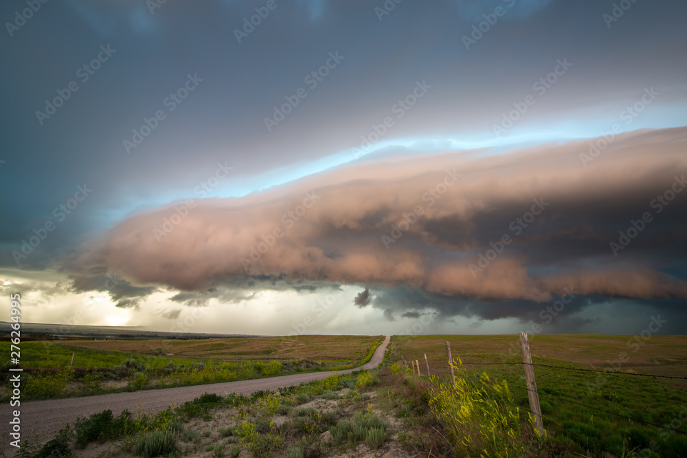 A dirt road in the countryside leads to the shelf cloud of a severe storm in the evening light.