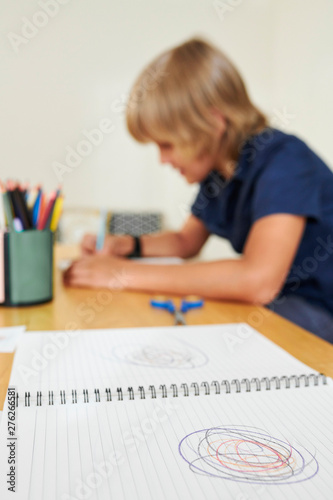 Desk with opened textbook with scribble and schoolboy drawing in background