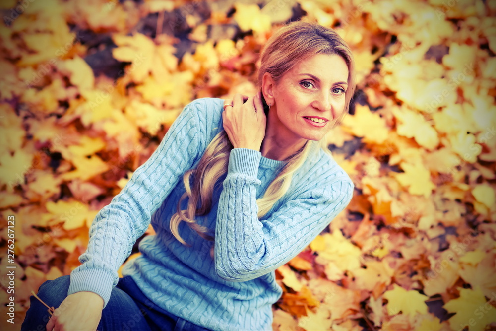 Happy beautiful blond woman in park on sunny autumn day toned. Smyling woman in blue sweater outdoors on beautiful fall day