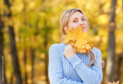 Happy beautiful blond woman in park on sunny autumn day toned. Smyling woman in blue sweater outdoors on beautiful fall day