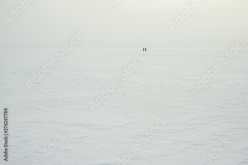 Figures of two travelers in the distance walking on the surface of a frozen lake covered with snow. Arctic landscape. High resolution and detail.
