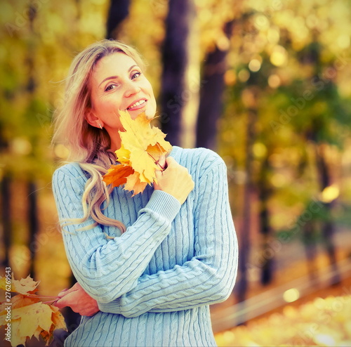 Happy beautiful blond woman in park on sunny autumn day toned. Smyling woman in blue sweater outdoors on beautiful fall day