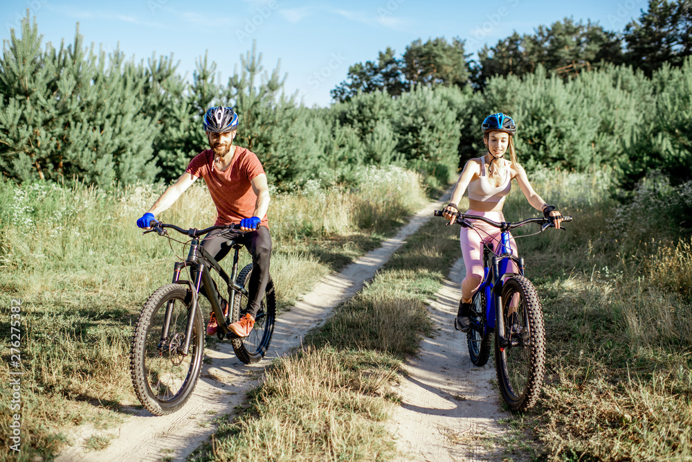Young man and woman riding mountain bicycles on the forest road during the summer time