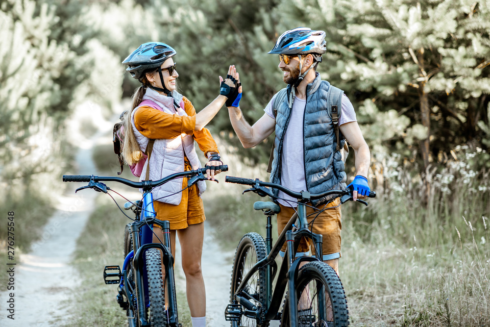 Young and active couple giving a five each other, having fun while traveling with bicycles on the forest road