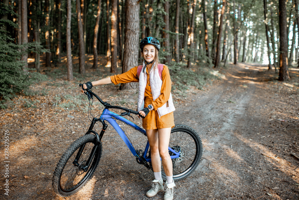 Portrait of a young woman with mountain bicycle in the forest - obrazy, fototapety, plakaty 