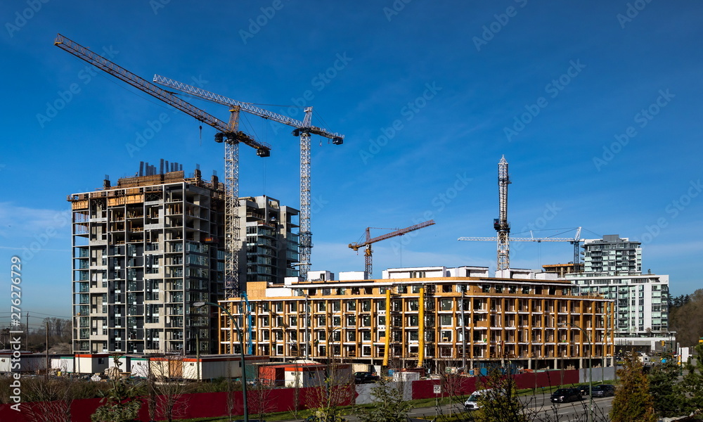 New construction of high-rise buildings in Burnaby city, industrial construction site, construction equipment, several construction cranes   on the background of finished skyscrapers and a clean blue 