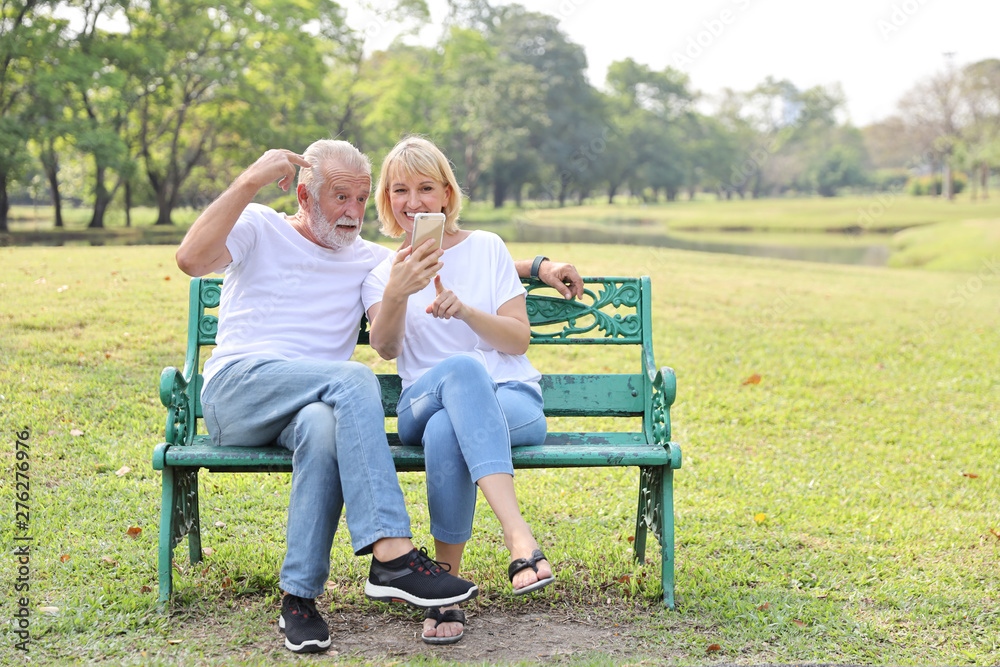 senior caucasian grandfather and grandmother sitting in park while using video call from smart phone to grandchildren with happy face and laughing senior caucasian grandfather and grandmother sitting in park while using video call from smart phone to grandchildren with happy face and laughing