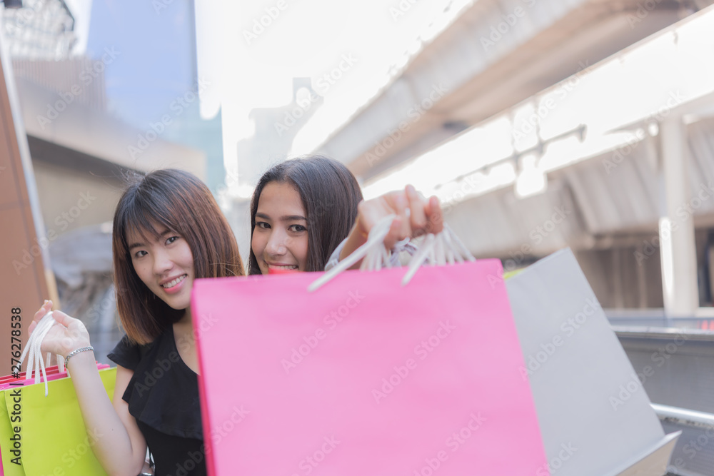 Happy asian girl friends with colourful paper bags  at shopping mall