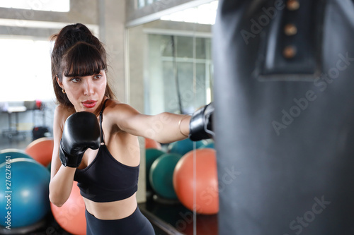 sporty caucasian girl in black sport with black boxer gloves, she punching sandbag with sexy red lip © feeling lucky