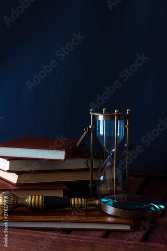 BOOKS ALONG TO CLOCK OF SAND AND MAGNIFYING ON WOODEN TABLE
