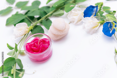 Red rose candle,beautiful butterfly pea flowers frame,green leaves and white stone on white background,top view