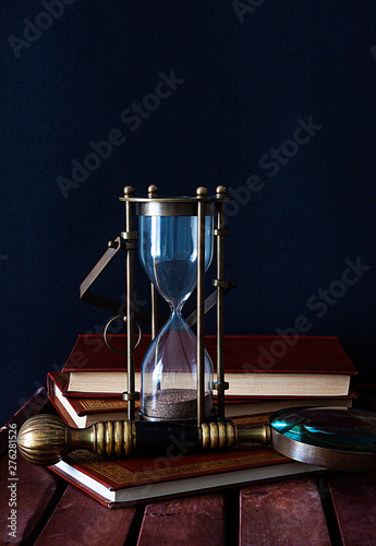 SAND CLOCK TOGETHER WITH BOOKS AND MAGNIFYING ON DARK BACKGROUND