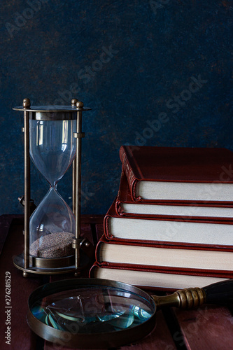 SAND CLOCK TOGETHER WITH BOOKS AND MAGNIFYING ON DARK BACKGROUND
