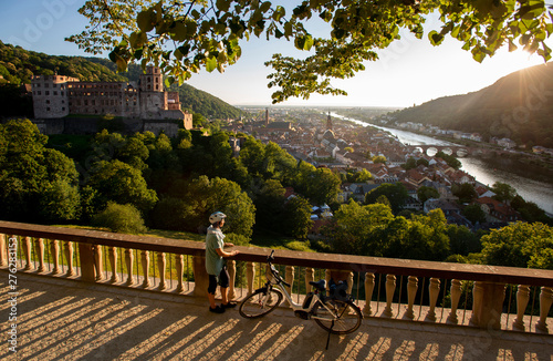 Fahrrad Fahrerin mit E-Bike blickt von der Scheffelterrasse in Heidelberg auf Schloss, Altstadt und alte Brücke, im Sonnen Abendlicht