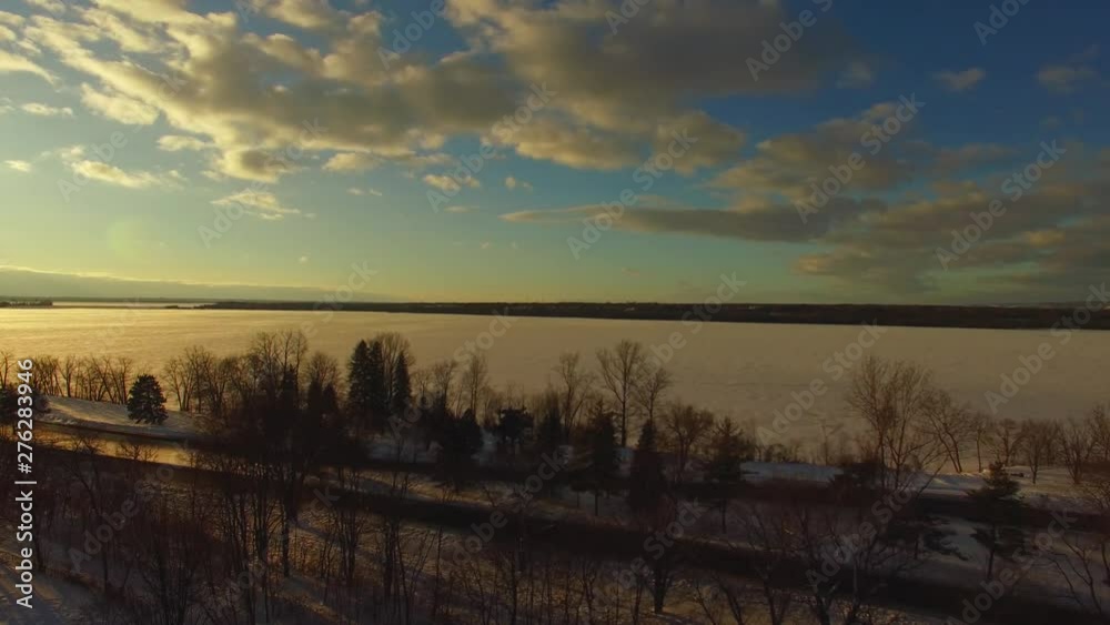 Drone flies over trees and looks over a frozen lake lit by the sunset. Drone flies over trees and looks over a frozen lake lit by the sunset.