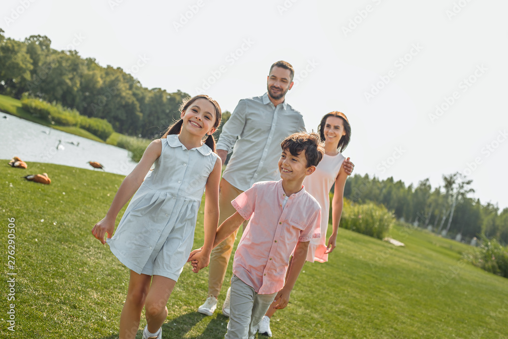 Happy kids. Young family of four holding hands, smiling and walking outdoors near the river Happy kids. Young family of four holding hands, smiling and walking outdoors near the river