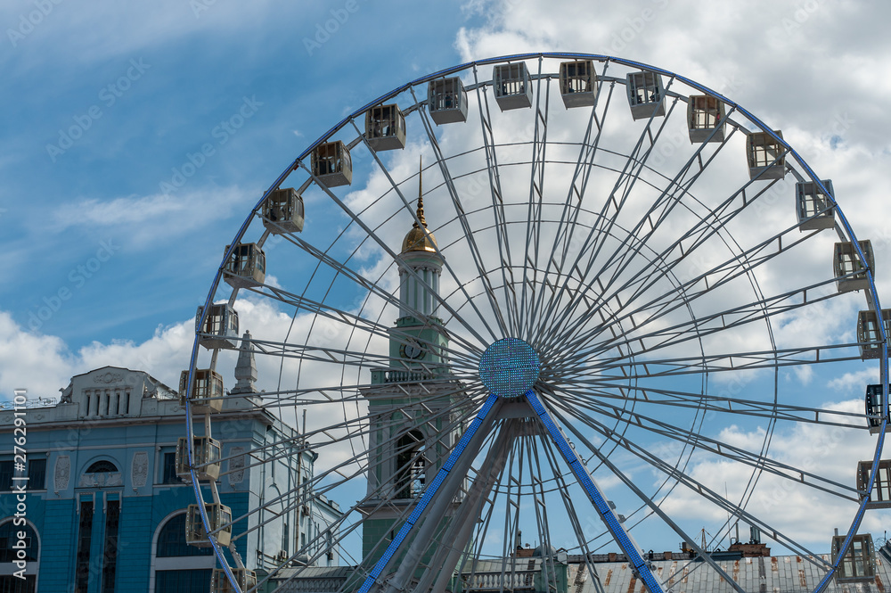 Part of big white Ferris wheel  and old church on the background under the blue sky with clouds, blue stylized photo, Kontraktova square at Podil, Kyiv
