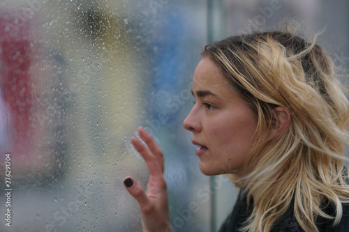 Woman looks through wet glass on a rainy day