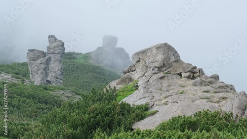 Summer mountain ridge with big vertical stony rocks. Wind with low clouds and fog. Carpathian, Chornohora, Vuhatyj Kaminj, Ukraine. photo