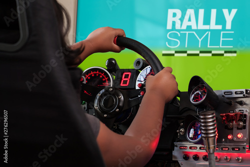 A girl playing a rally game holding a steering wheel from a racing sim cockpit and turning the wheel towards the right.