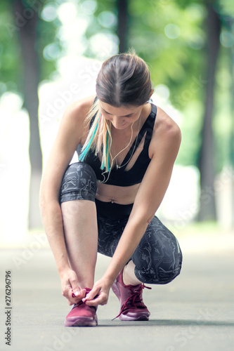 Front view woman is tying shoelaces before runing in the city park. Fitness and lifestyle concept.