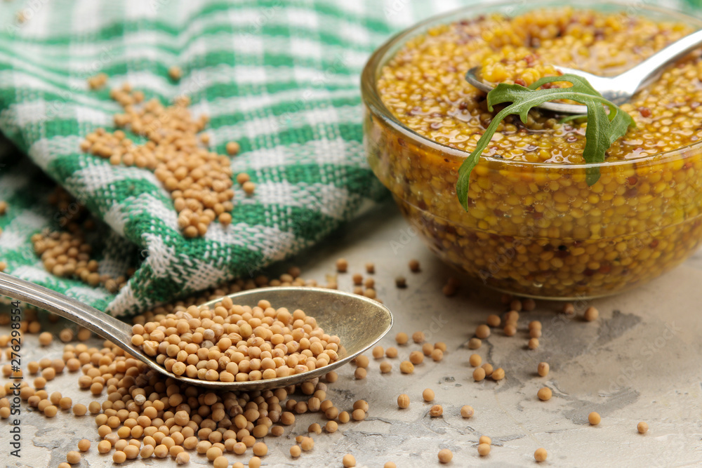 Mustard sauce, French Mustard in a bowl and dry grains on a light concrete table. close-up. Mustard sauce, French Mustard in a bowl and dry grains on a light concrete table. close-up.