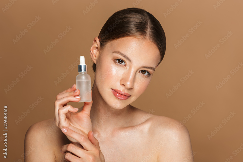 Beautiful pleased young amazing woman posing isolated over brown chocolate background wall holding oil drop serum.