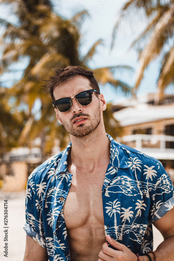 Handsome mature male model enjoying a sunny day on the beautiful island of Boracay. Walking with open blue shirt between palm trees on famous white beach.