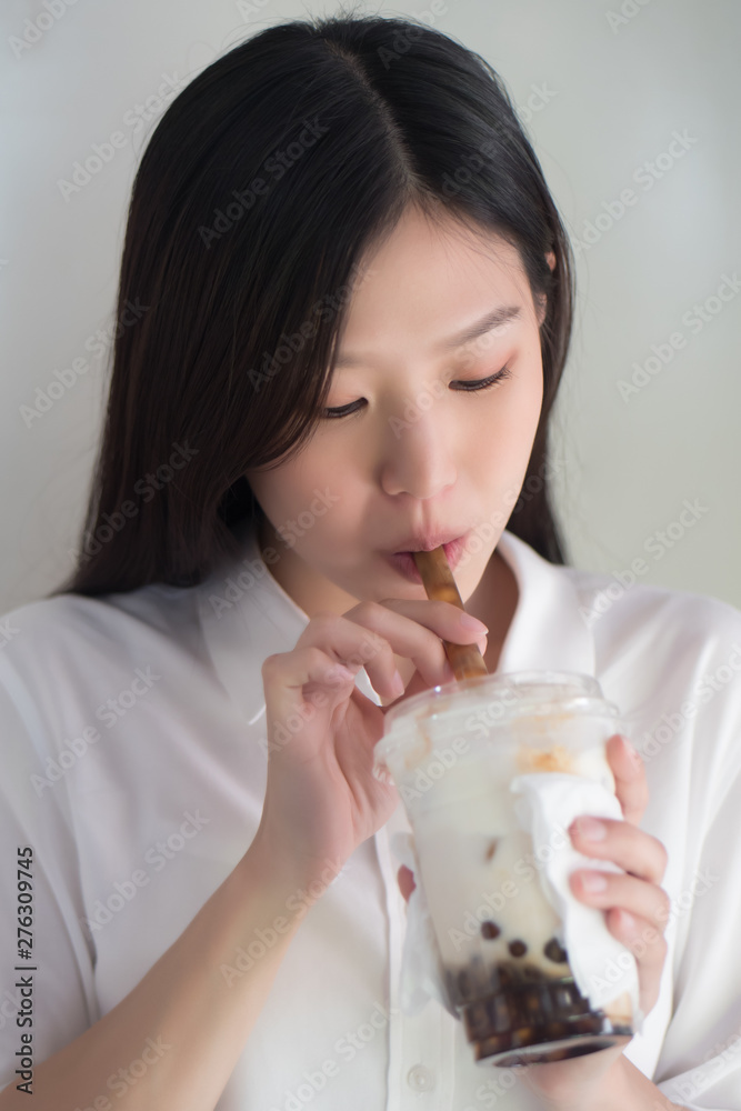Asian woman drinking iced bubble milk tea; aka boba tea, pearl milk tea, tapioca tea, asian exotic beverage concept Asian woman drinking iced bubble milk tea; aka boba tea, pearl milk tea, tapioca tea, asian exotic beverage concept