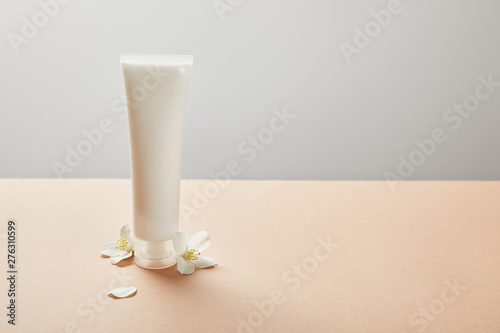 cream tube with cream and few jasmine flowers on beige isolated on grey