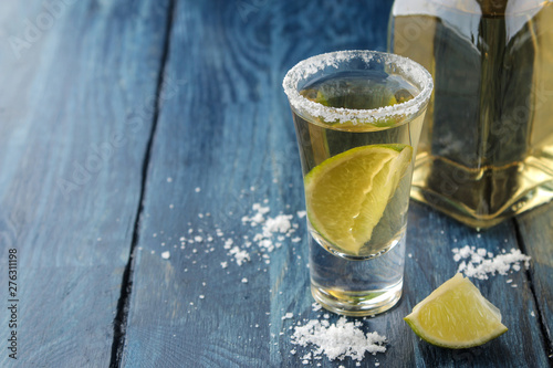 Gold tequila in a glass with salt and lime on a blue wooden table. alcoholic beverages.