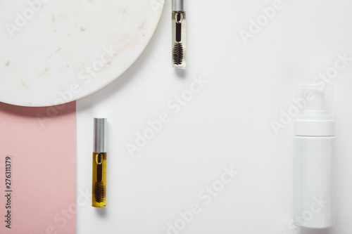 top view of mascara bottles and cosmetic dispenser near plate on white pink surface