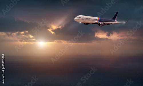 the plane of rainbow color flies in the stormy sky with the evening light of the sun. the plane flies over the dark sea