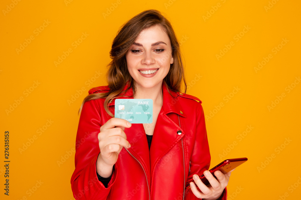 Happy young woman holding credit card on standing on the yellow background Happy young woman holding credit card on standing on the yellow background